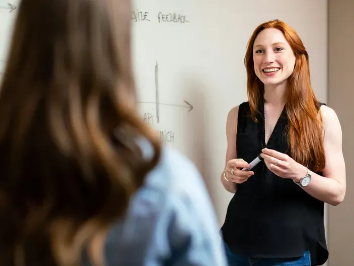 Confident businesswoman smiling while presenting ideas to colleague near whiteboard during team meeting